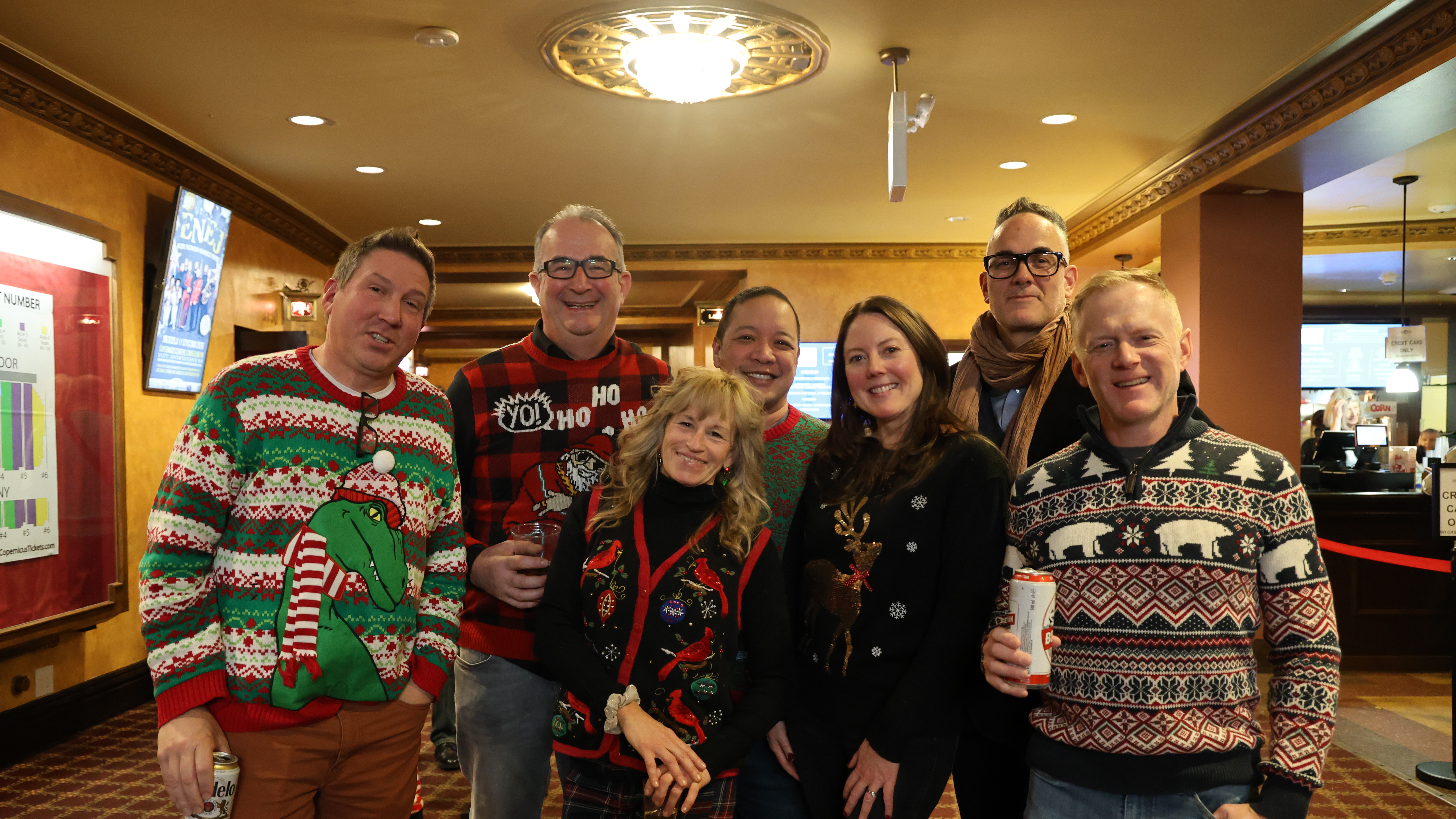Photograph of seven people in ugly Christmas sweaters.